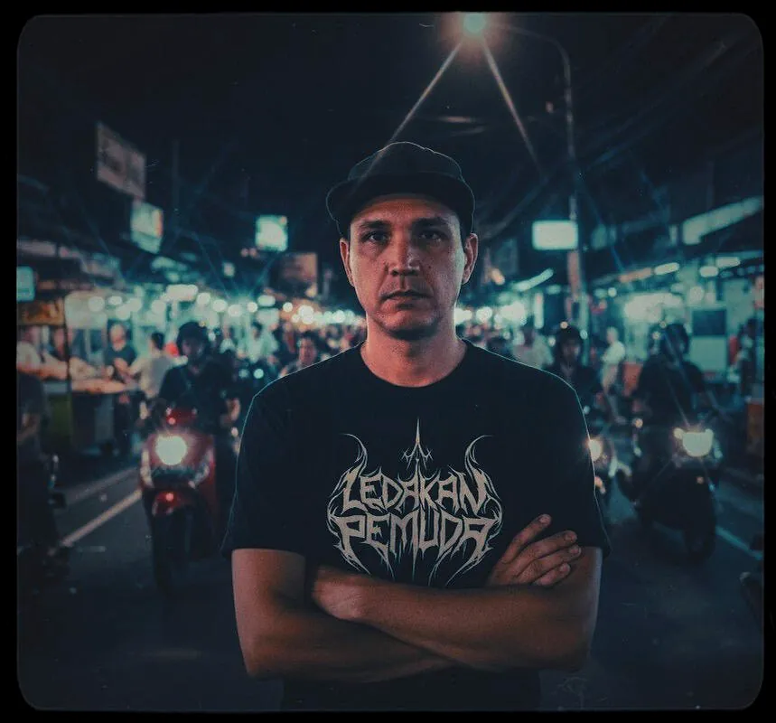 Patrick Padgett bersedekap mengenakan topi pet dan kaus berlogo Ledakan Pemuda di jalan Jakarta pada malam hari